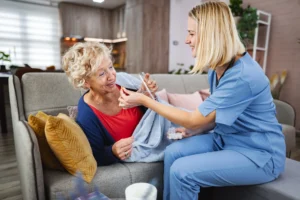 Caregiver assisting an elderly woman with medication at home in a comfortable living room setting.